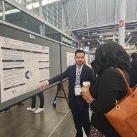 Image shows Dr. Solorzano at a conference providing information to a fellow attendee on the Impact of Medicaid Policy Change on CGM Uptake Federally Qualified Health Center.